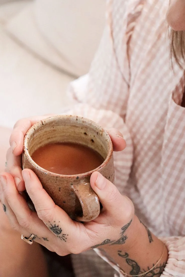 Mãos com tatuagens segurando uma caneca de cacau